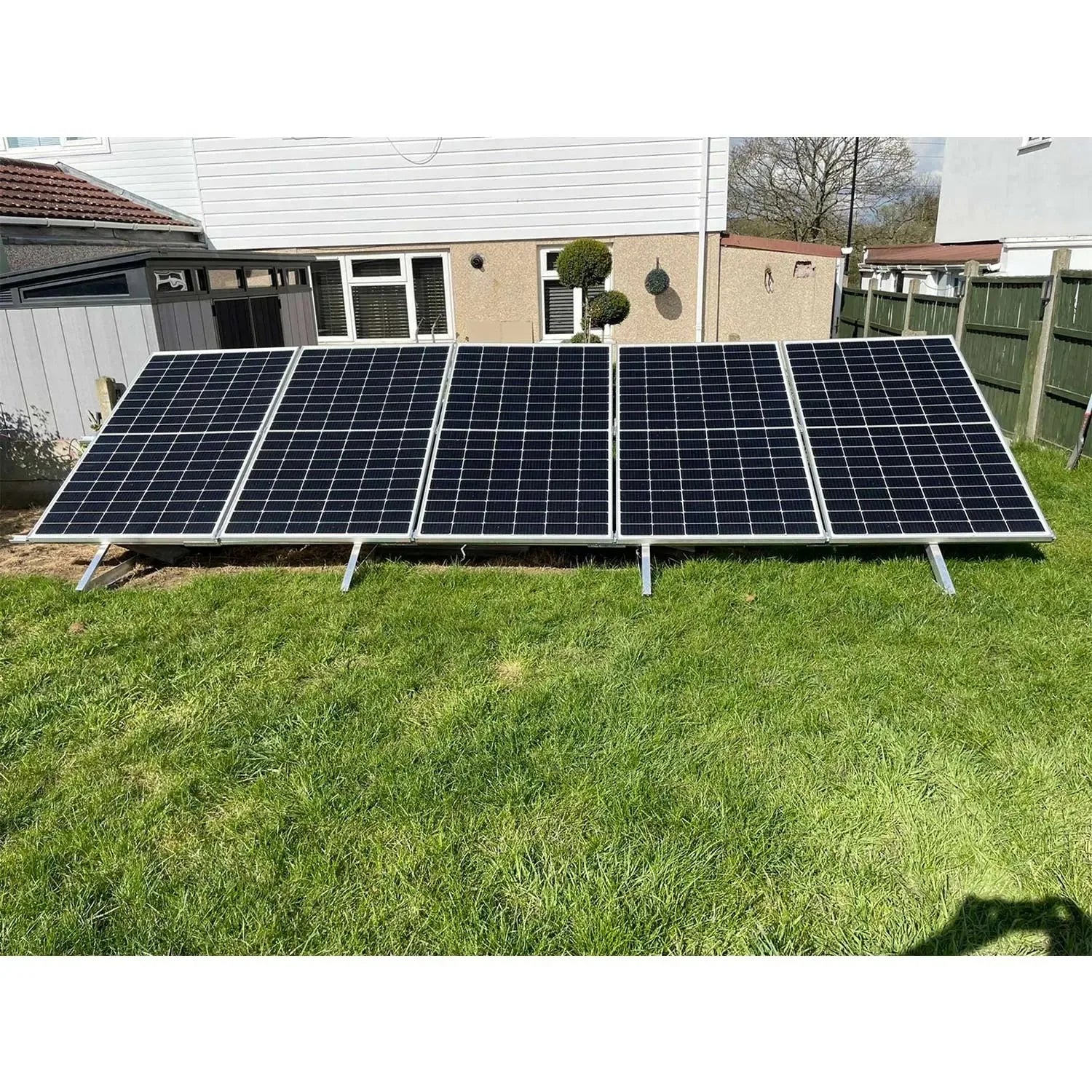 Five solar panels mounted on aluminum triangle frames in a residential backyard on grass.