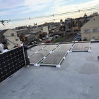 Solar panel mounting brackets installed on flat rooftop with multiple panels secured in white ABS stands overlooking resident