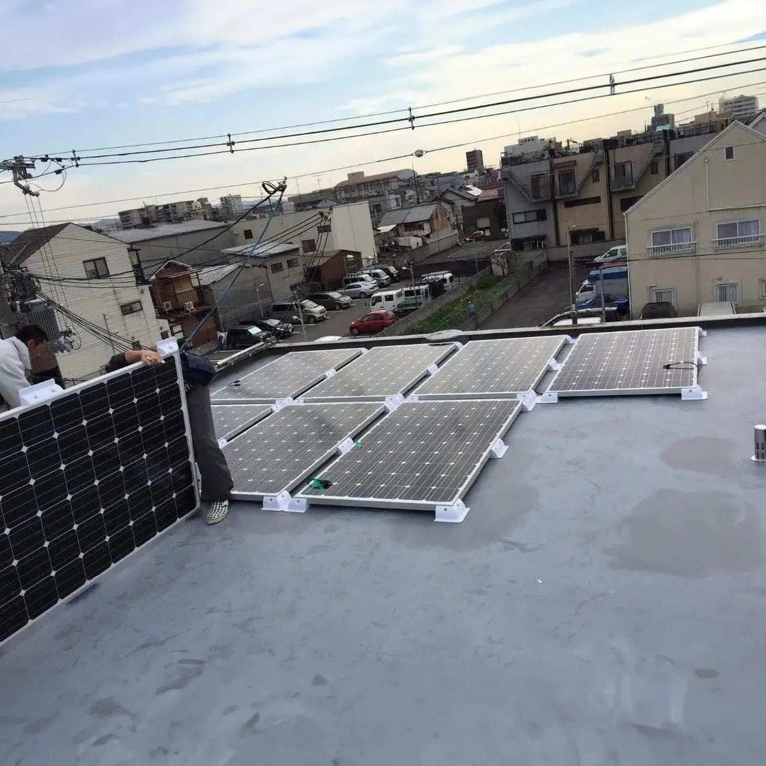 Solar panel mounting brackets installed on flat rooftop with multiple panels secured in white ABS stands overlooking resident