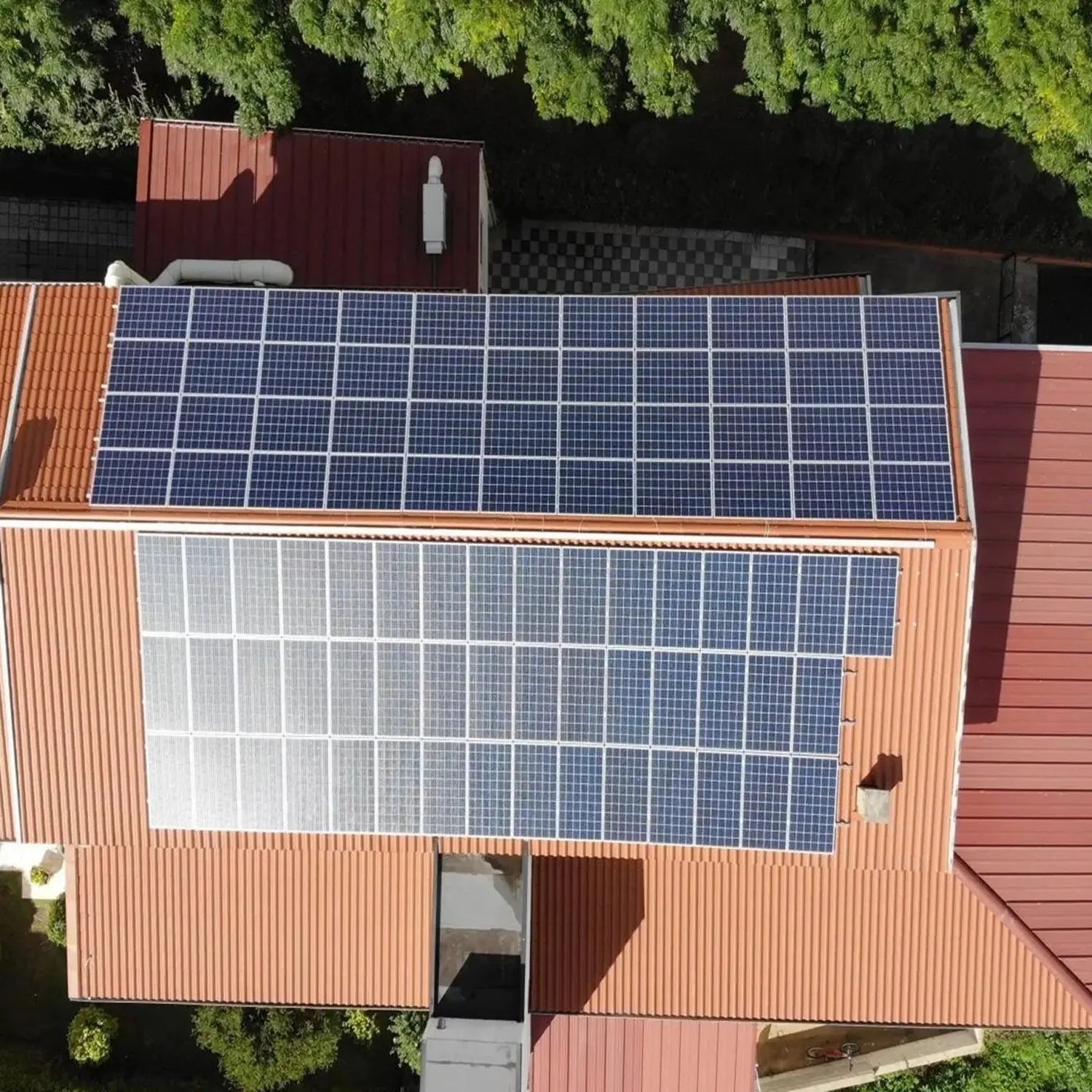 Aerial view of corrugated metal building with solar panels mounted on roof and landscape tile roof mounting system installed.