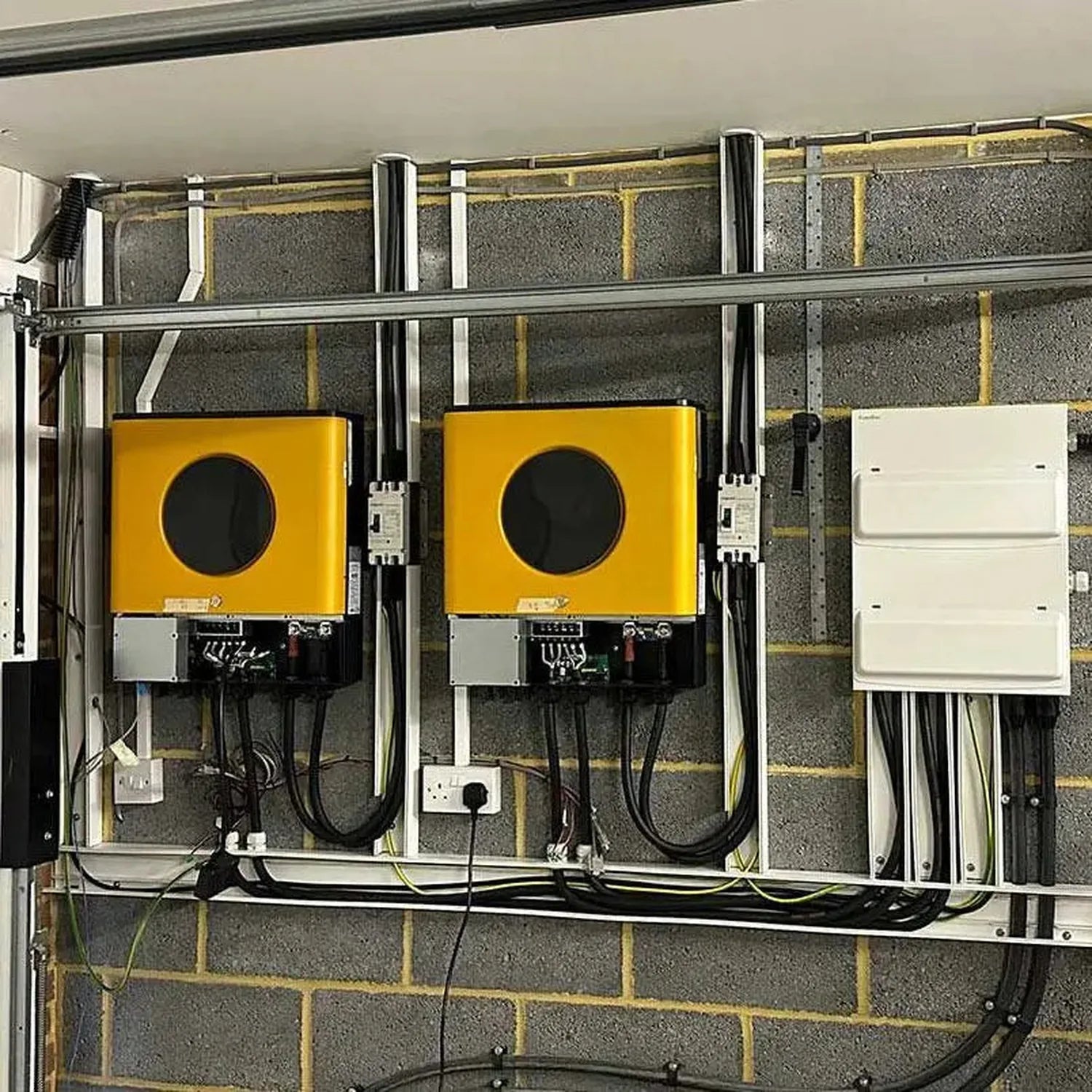 Two yellow solar inverter chargers mounted on wall-mounted metal frame with control panels, wiring, and white electrical box 