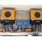 Installation shot of two orange and black Voltacon Energy Systems inverters mounted on brick wall with blue charge controller