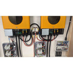 Dual yellow solar inverter chargers with black control panels mounted above three electrical distribution boxes with circuit 