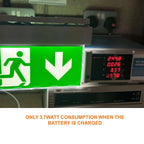 Green LED emergency exit sign with downward arrow, mounted above digital power meter displaying 3.7 watts consumption when ba