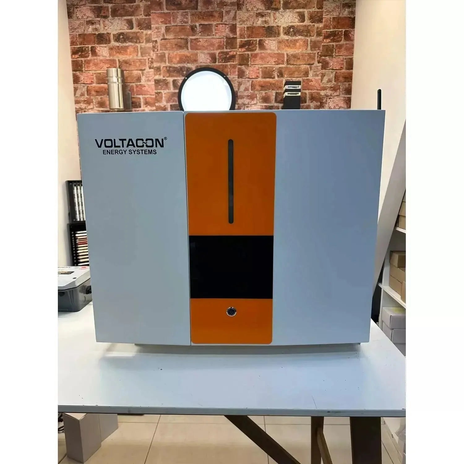 Voltagon Energy Systems hybrid inverter charger with blue side panels and orange center section, displayed on white table aga