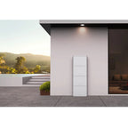 White stacked battery unit mounted on pink wall of modern home exterior overlooking landscape.