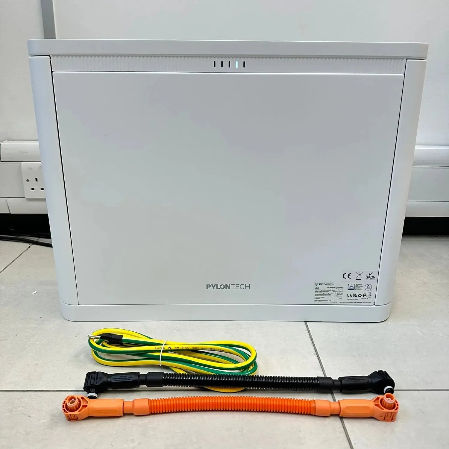 Pylontech Pelio-L battery unit displayed with three colored cable connectors on white tile floor.