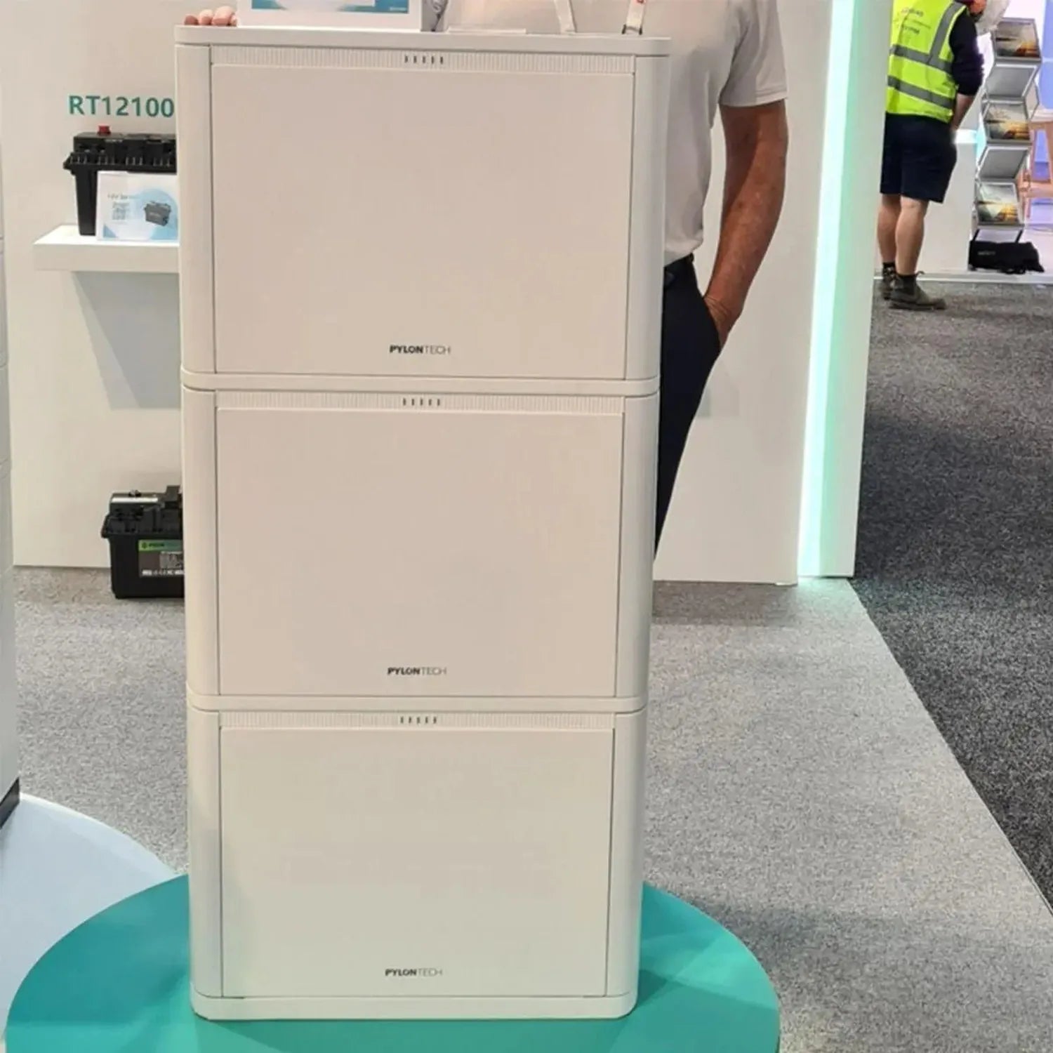 Three-unit stacked Pylontech Pelio-L battery modules displayed in a showroom with RT12100 controller shown on shelf above.