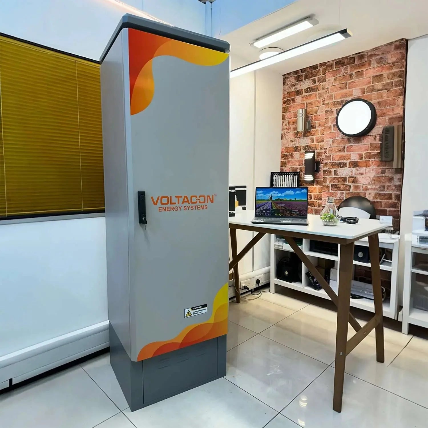 Voltacon Energy Systems battery enclosure installed in an office showroom with exposed brick wall and work desk.