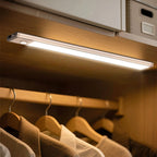 Sleek LED under-cabinet light mounted on wooden shelf, illuminating hanging wooden hangers with clothing below, demonstrating