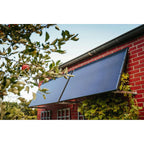 Blue solar panel mounted on red brick building with black metal frame and surrounding foliage.