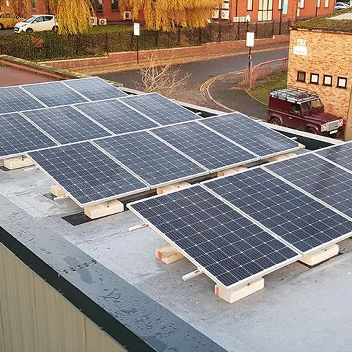 Adjustable solar panel mounting system installed on flat commercial roof with multiple panels at tilted angles, urban setting