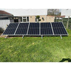 Five solar panels mounted on adjustable ground stands in a residential garden, angled toward the sun.