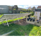 Adjustable solar panel mounting kit installed in residential garden, angled toward sun with white aluminum frame and black pa