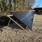 Adjustable solar panel mounting kit installed on gravel ground with panels angled toward sunlight, trees and farm buildings v
