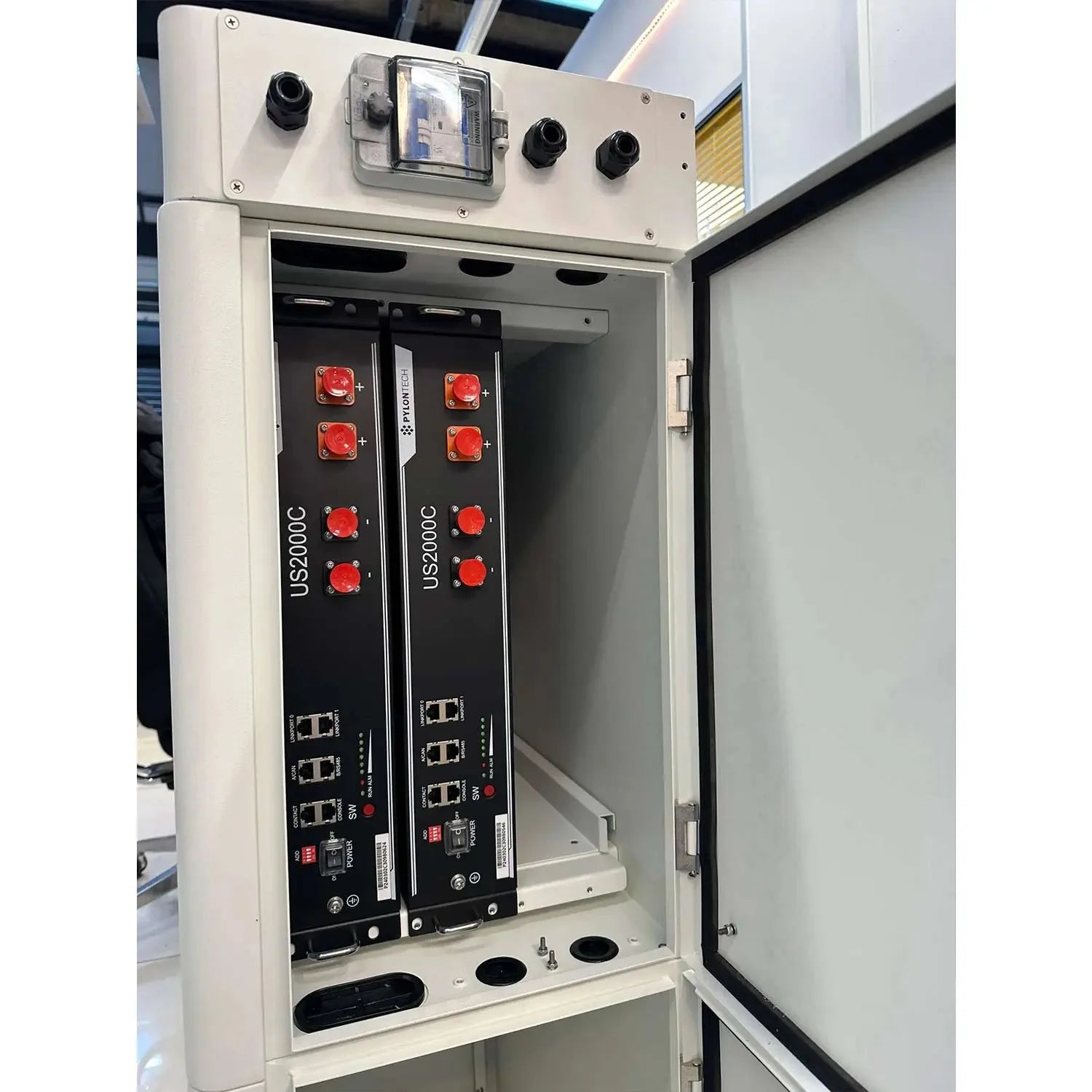 Open white cabinet showing two black Pylontech US2000C battery modules with red indicator lights and network ports inside.