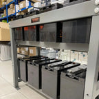 Voltagon energy system steel mounting rack displaying eight stacked 6V batteries with black tops in warehouse setting.
