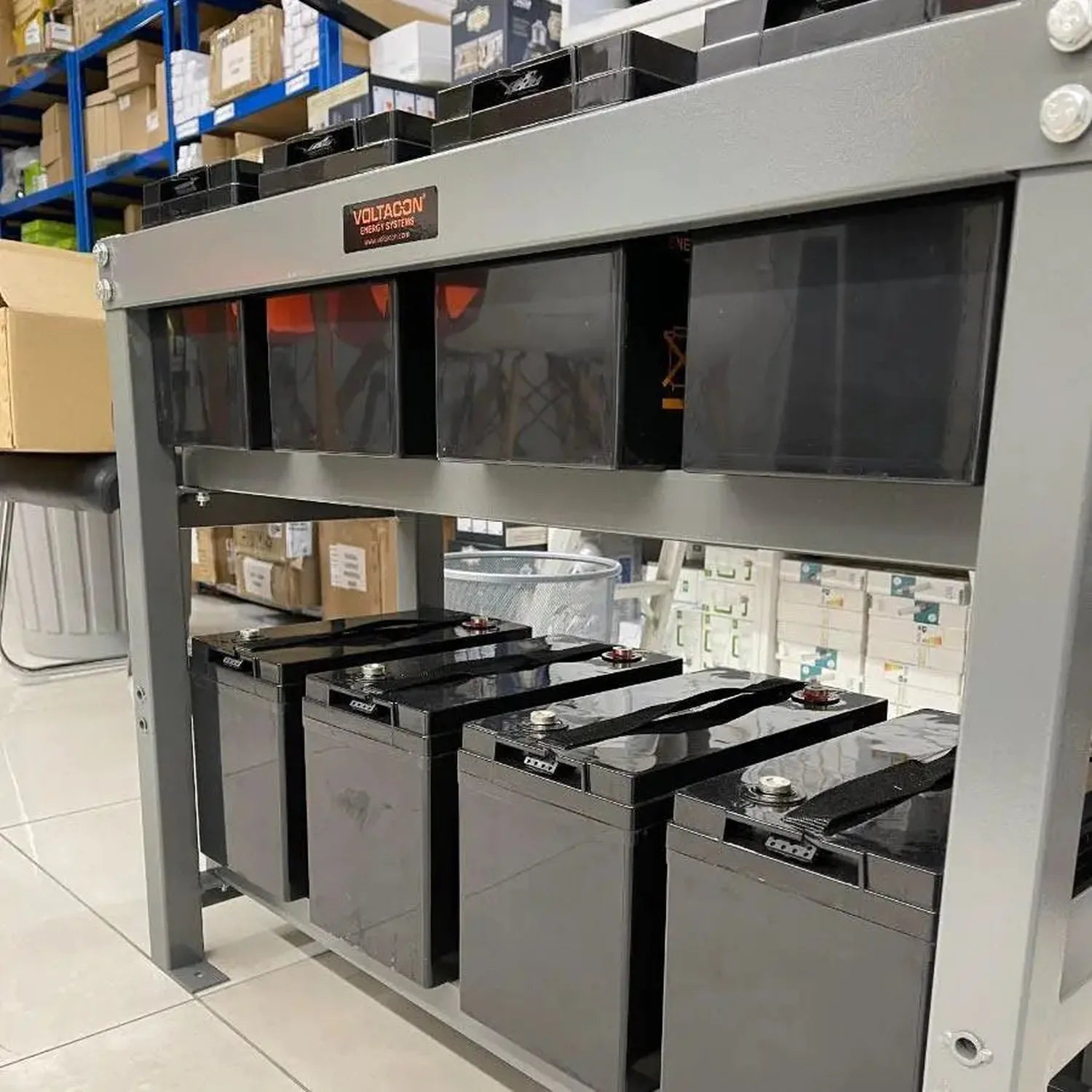 Voltagon energy system steel mounting rack displaying eight stacked 6V batteries with black tops in warehouse setting.
