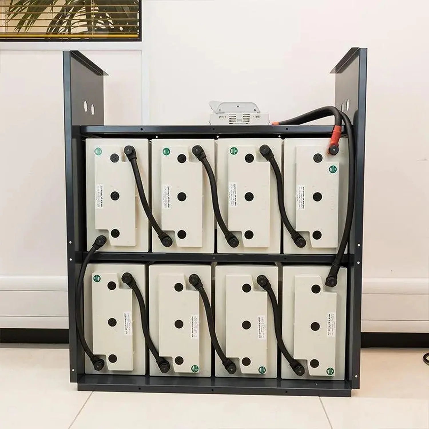 Black metal rack mounted with eight cream-colored battery units arranged in two rows, each with black cables and connectors, 