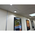 Recessed LED ceiling light installed in office hallway with drop ceiling tiles, illuminating wall-mounted energy posters belo