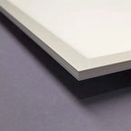 Close-up of LED panel light edge showing white frame and visible paper layers against gray surface.