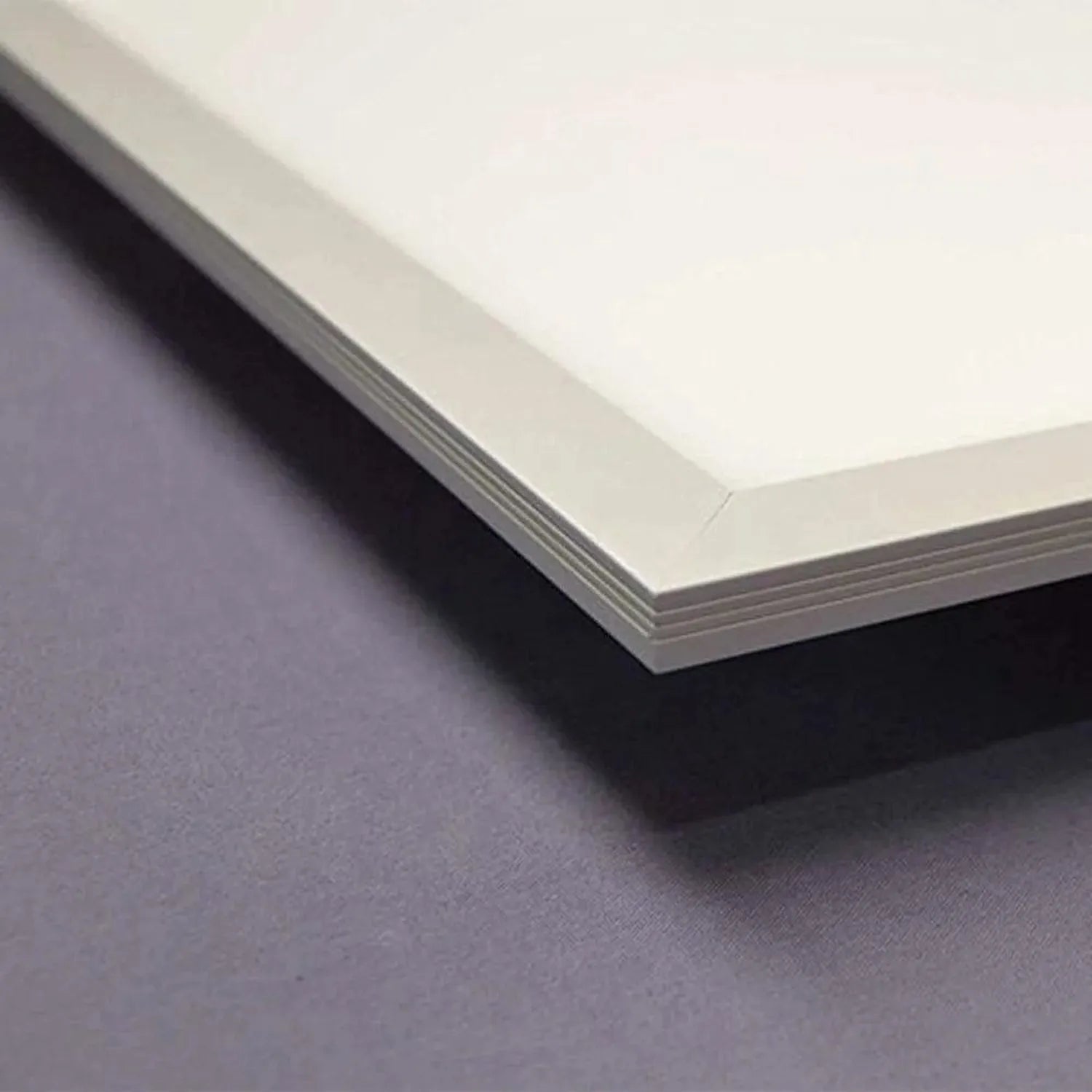 Close-up of LED panel light edge showing white frame and visible paper layers against gray surface.