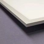 Close-up of an LED panel light edge showing white face, aluminum frame, and layered internal structure on gray surface.
