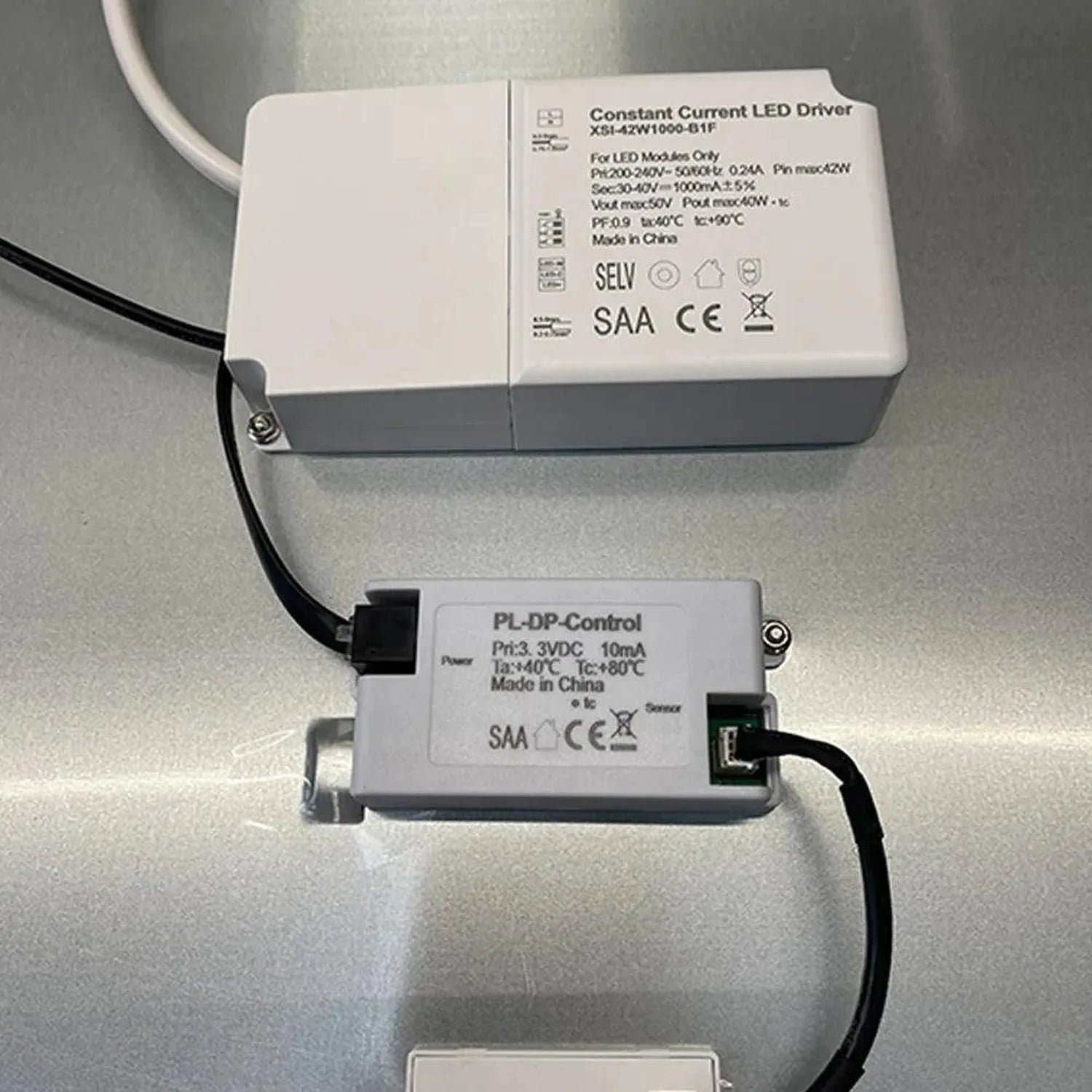 Two white LED driver modules with cables displayed on gray surface, showing specifications and certification labels.