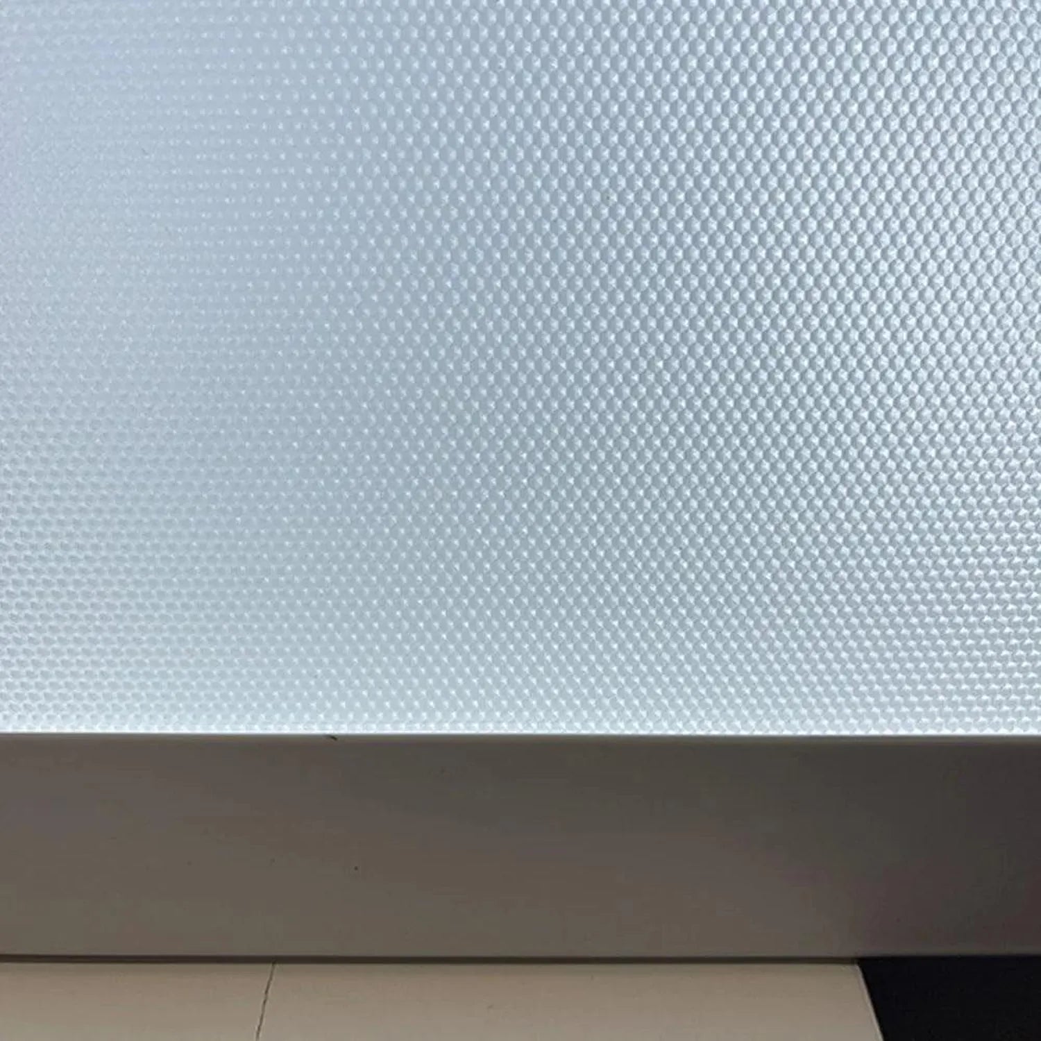 Close-up of textured white LED panel surface showing dimpled grid pattern, mounted against dark frame edge.