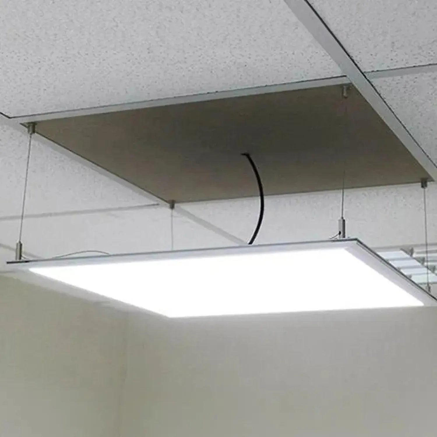 Modern LED panel suspended from ceiling with cable kit installed, showing bright white illumination and metal mounting hardwa