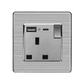 Brushed steel wall socket with single outlet, toggle switch, USB-A port, and USB-C port against textured background.