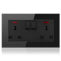 Black tempered glass electrical outlet plate with two switched sockets, USB ports, and red indicator lights against gray back