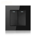 Black tempered glass 2-gang light switch with two rectangular buttons and indicator lights, mounted on wall plate.