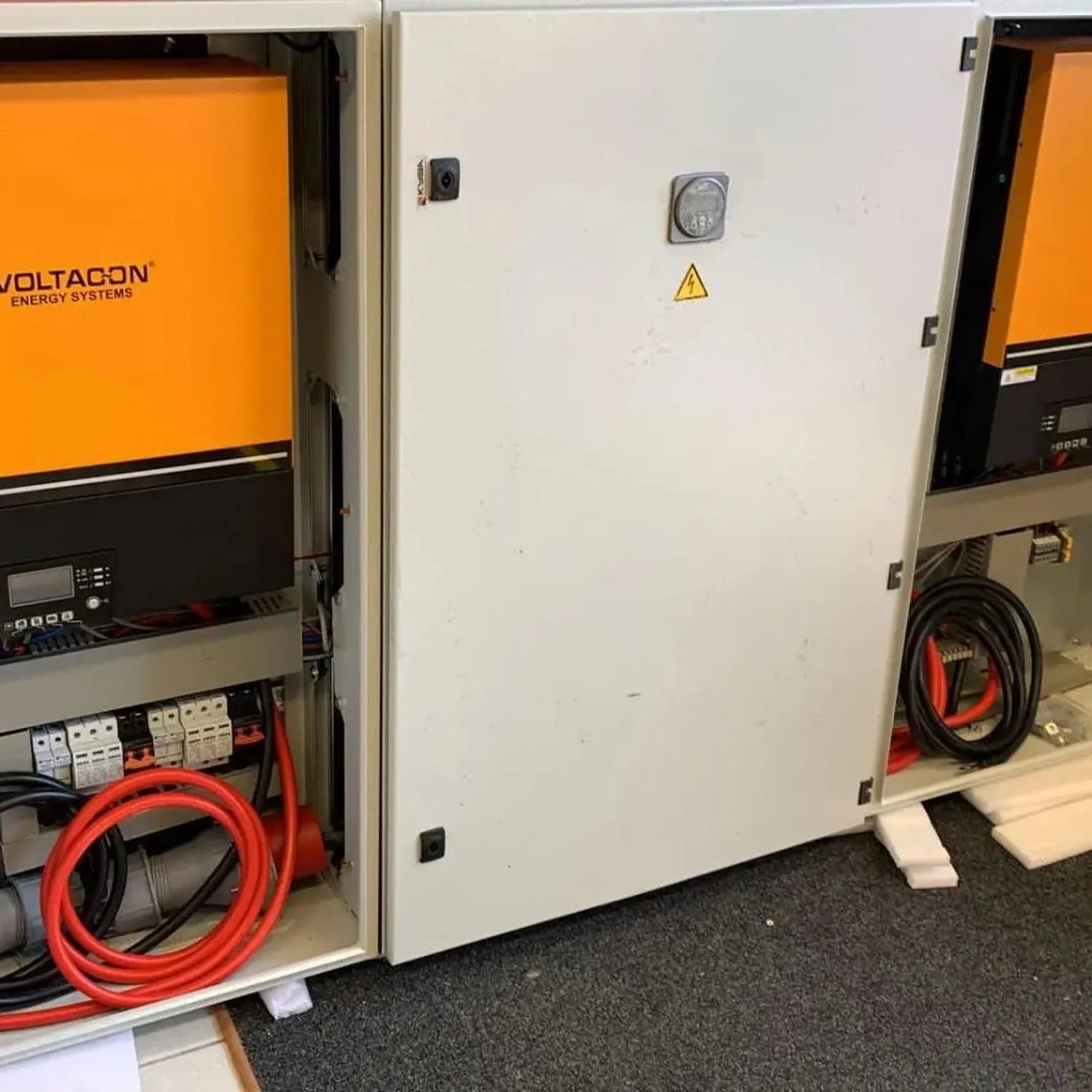 Three Voltagen energy systems cabinets installed side by side, featuring orange doors and control panels with red power cable