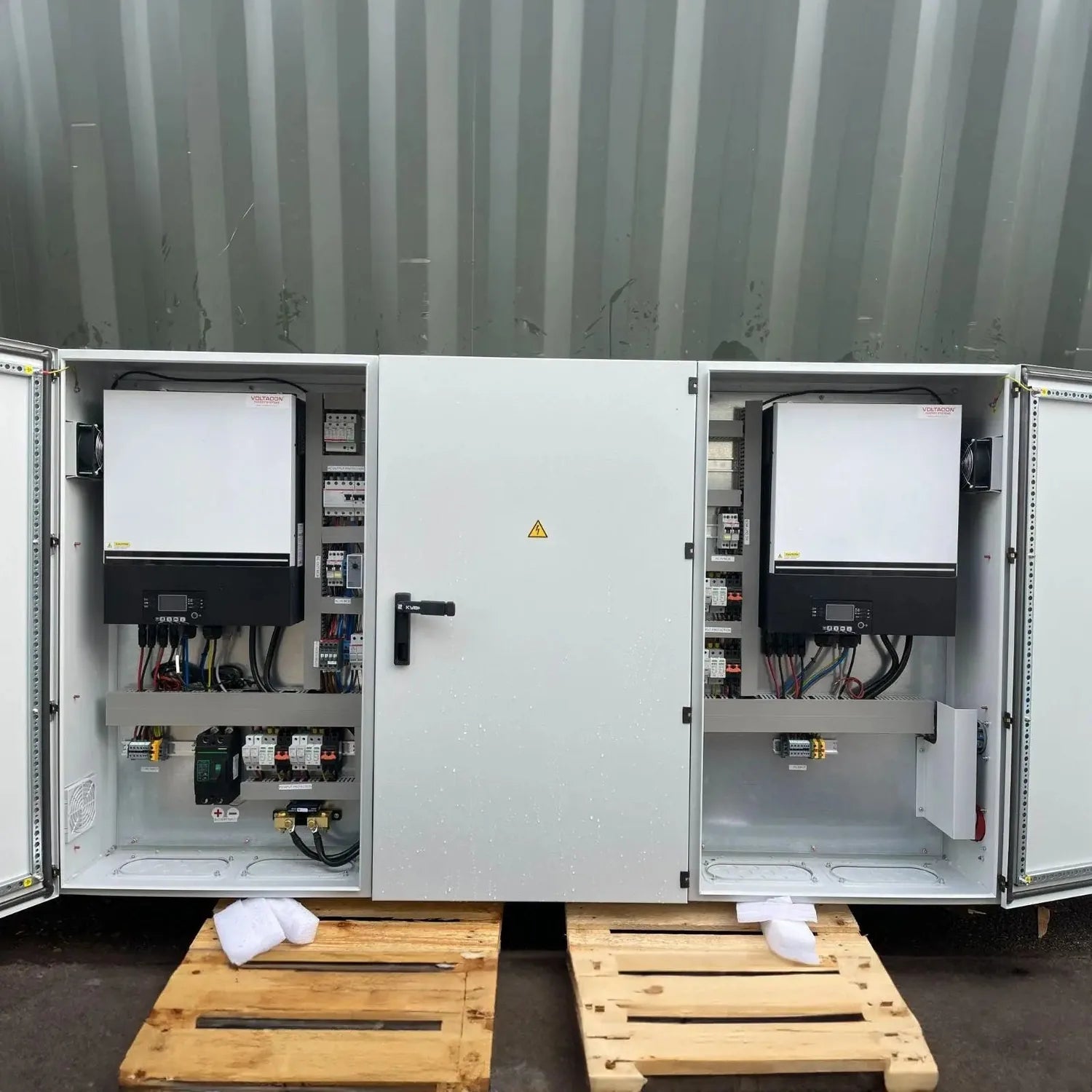 Pair of open electrical cabinets with inverters and circuit components mounted inside, displayed on wooden pallets against co