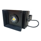 Black LED flood light with yellow-centered lamp, adjustable barn doors, and power cable against white background