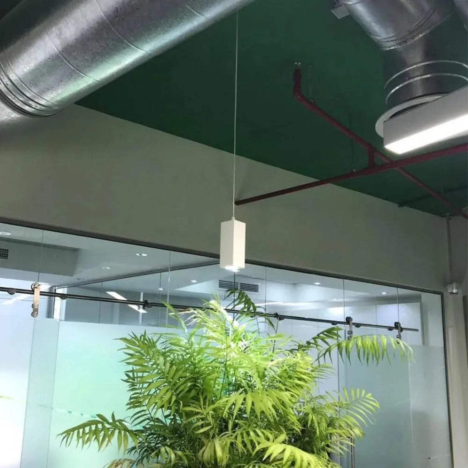 White pendant LED downlight suspended in modern office space with glass partitions and industrial ceiling.