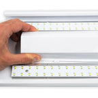 Hand holding edge of white LED ceiling light fixture showing dual rows of yellow LED chips mounted on aluminum rails inside w
