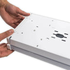 Hands holding a white rectangular LED ceiling light fixture showing mounting holes and ventilation slots on its underside.