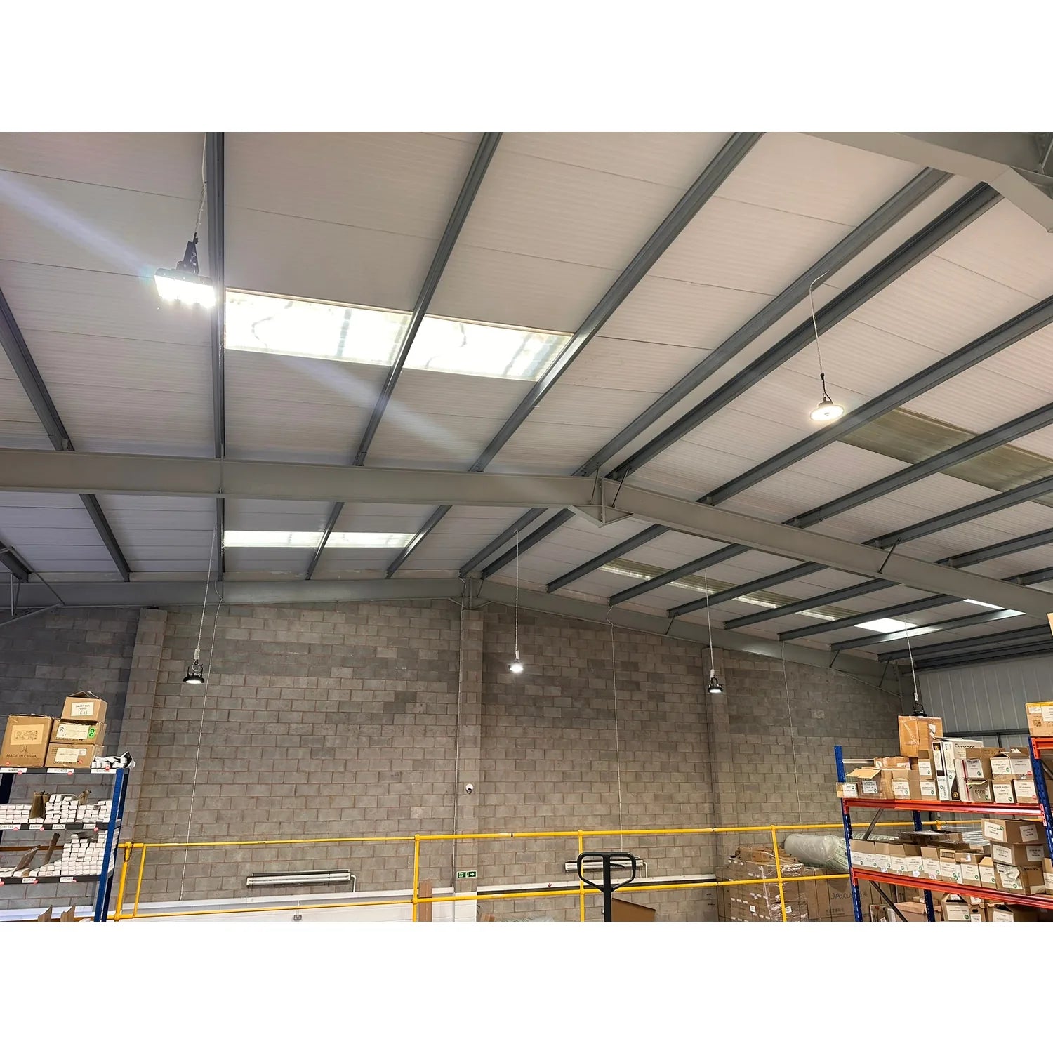 Industrial warehouse ceiling with LED high bay lights mounted on steel beam structure above storage racks.