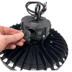 Hand holding adjustment knob on underside of black LED high bay light fixture with radiating fins and mounted cable harness.