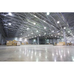 Empty warehouse interior with concrete floor, metal beam ceiling structure, and LED high bay lights illuminating the space wi