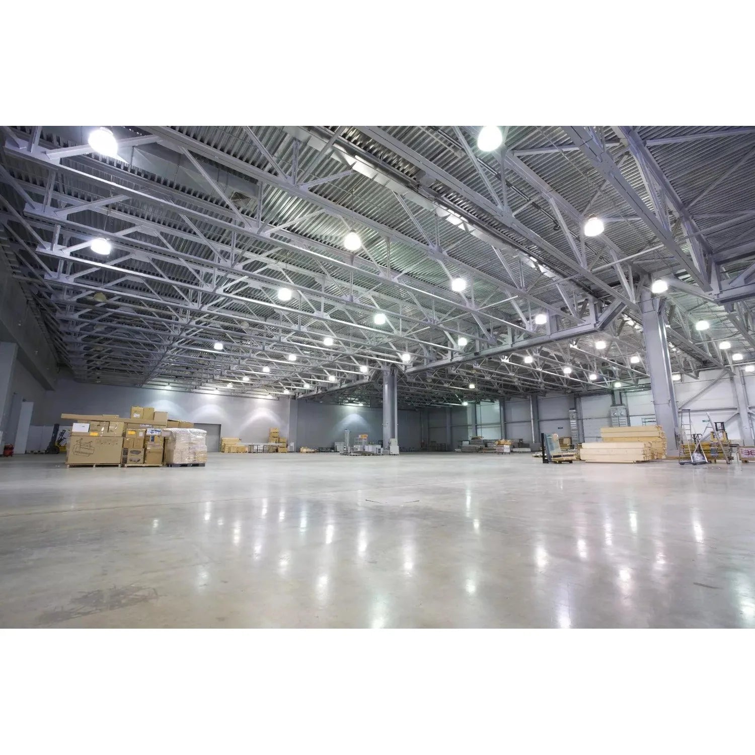 Empty warehouse interior with concrete floor, metal beam ceiling structure, and LED high bay lights illuminating the space wi