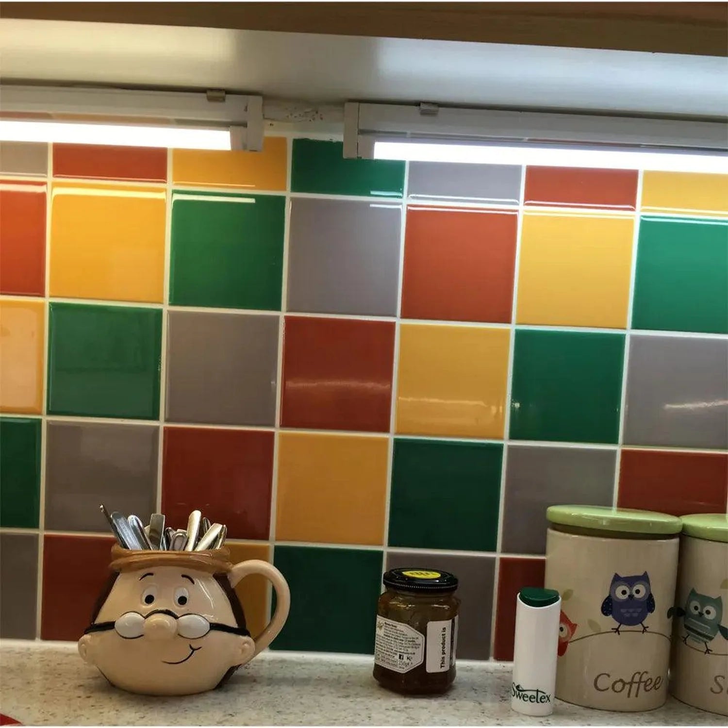 Colorful tile backsplash with LED under-cabinet lighting installed above kitchen counter, displaying utensil holder and decor