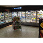 Refrigerated grocery store section with glass-door freezers stocked with frozen foods and beverages, fluorescent lighting ove