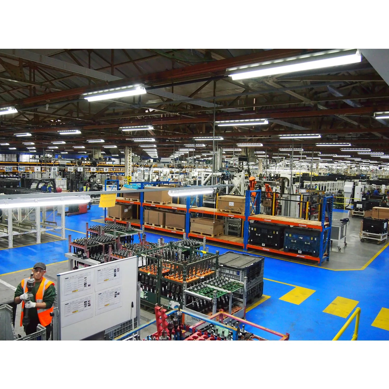 Industrial manufacturing facility with LED tube lighting installed overhead throughout the warehouse space, illuminating work