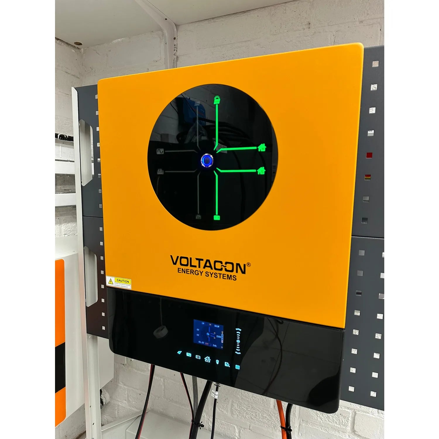 Voltacon Energy Systems inverter mounted on white brick wall, displaying green diagnostic interface on circular black screen 
