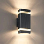 Black ribbed cylindrical LED wall light mounted on white wall, emitting warm light upward and downward.