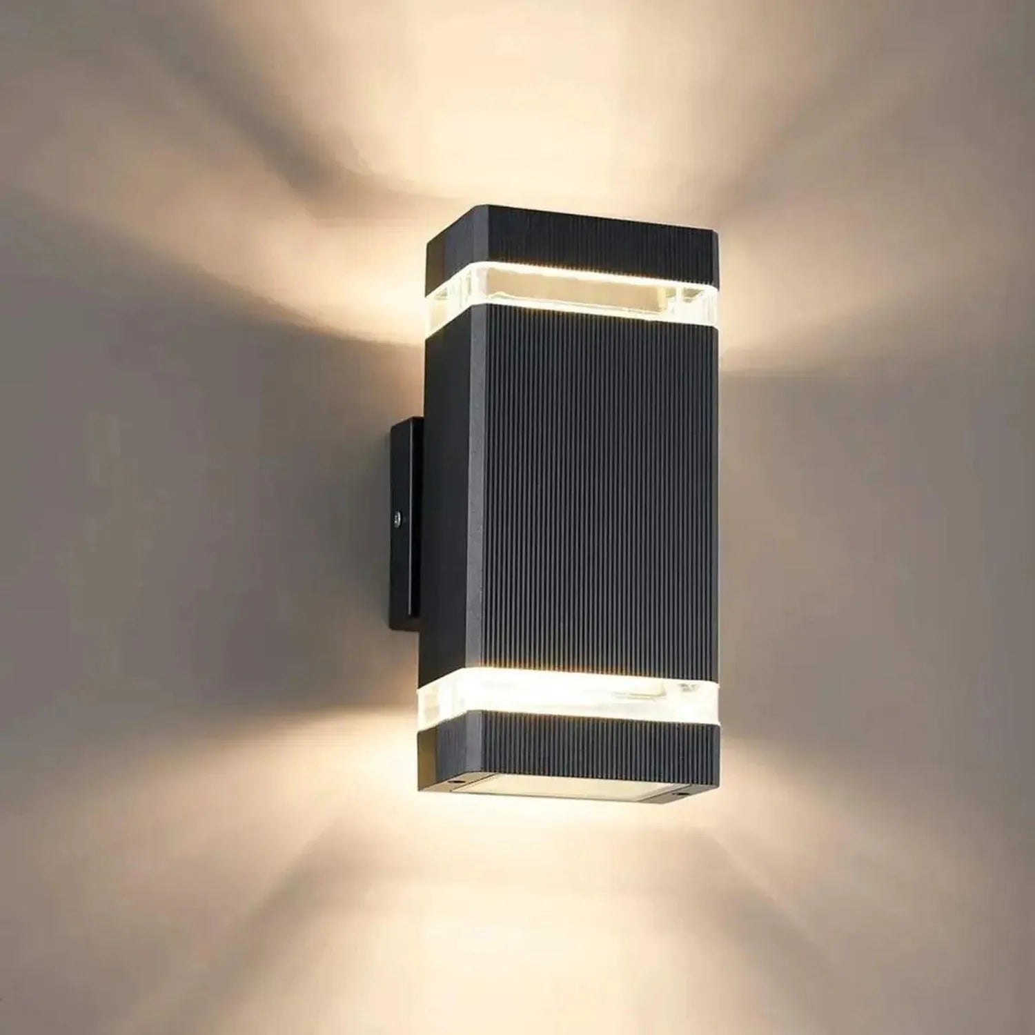 Black ribbed cylindrical LED wall light mounted on white wall, emitting warm light upward and downward.