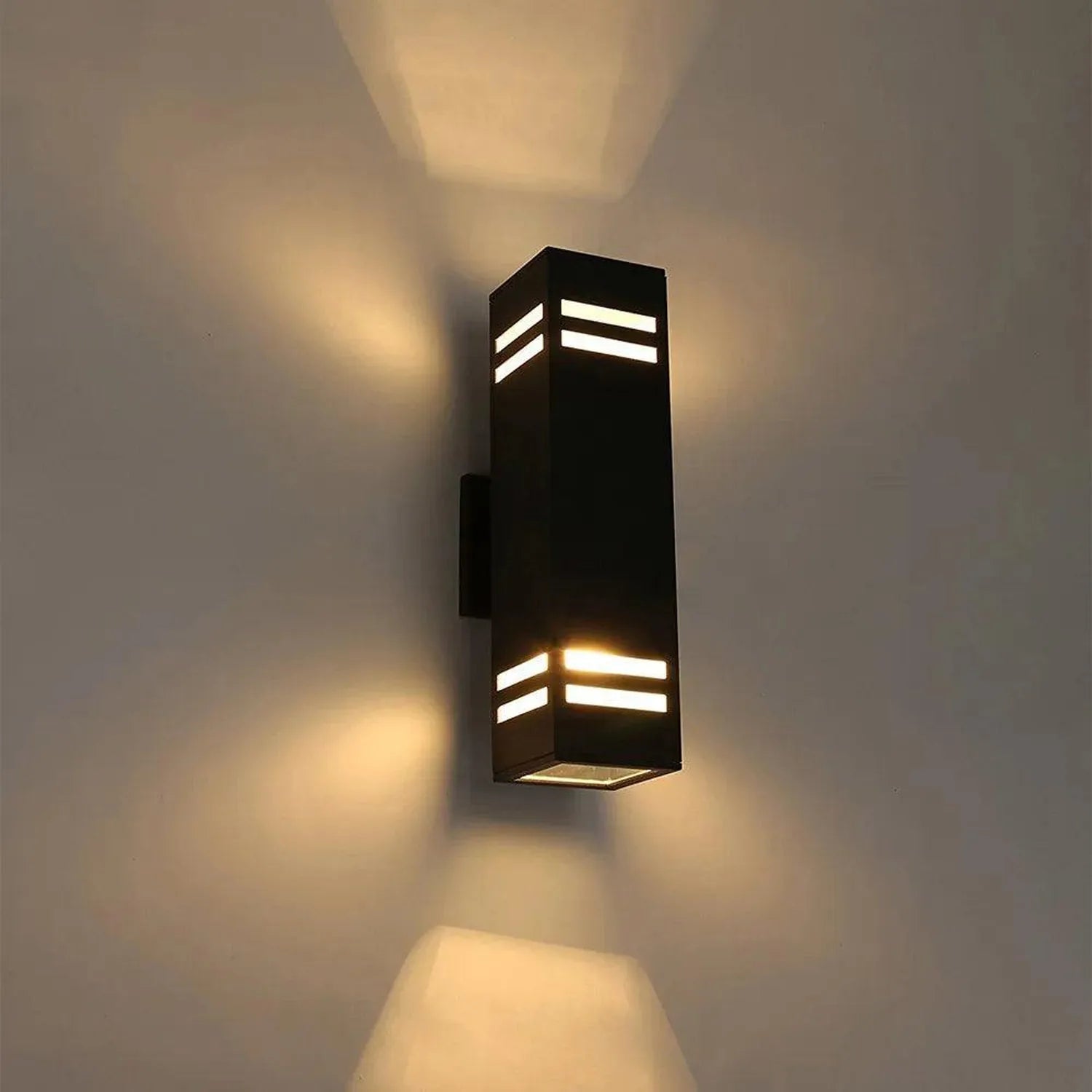 Modern black rectangular wall sconce with horizontal light slots, mounted on cream wall, casting warm ambient light above and